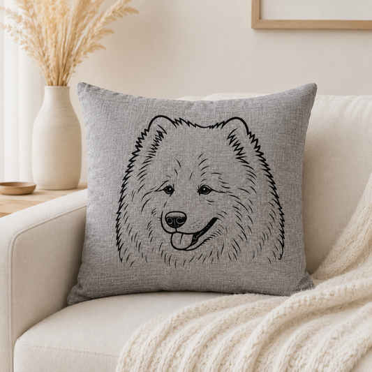 A square grey throw pillow with a black line art illustration of a fluffy dog face, resting on a cream-colored sofa with a knit blanket.