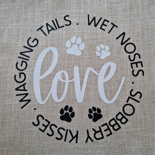 A beige cushion cover with the word 'love' and dog-related phrases such as 'wagging tails', 'wet noses', and 'slobbery kisses' printed on it, along with paw prints - dog gift in Australia made by Rieko's World.