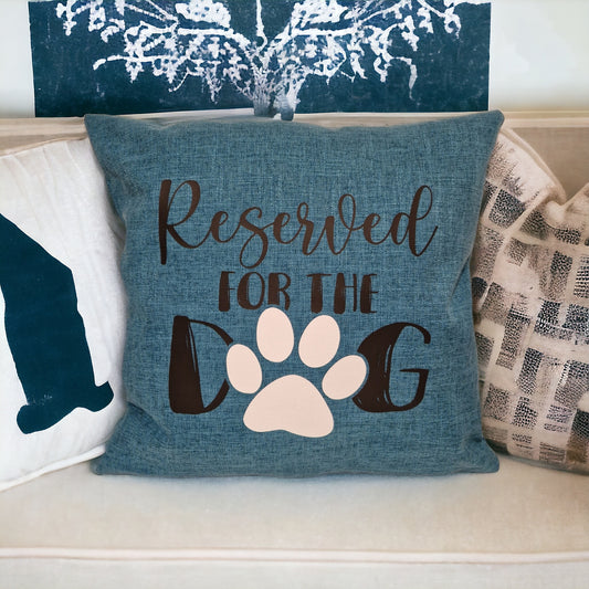 A close up of a teal cushion cover on cream sofa with other printed cushions with 'Reserved for the Dog' text and a paw print design. In Australia by Rieko's World.