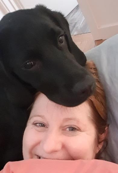 Becs, founder of Rieko’s World, cuddling black Labradoodle Rieko.