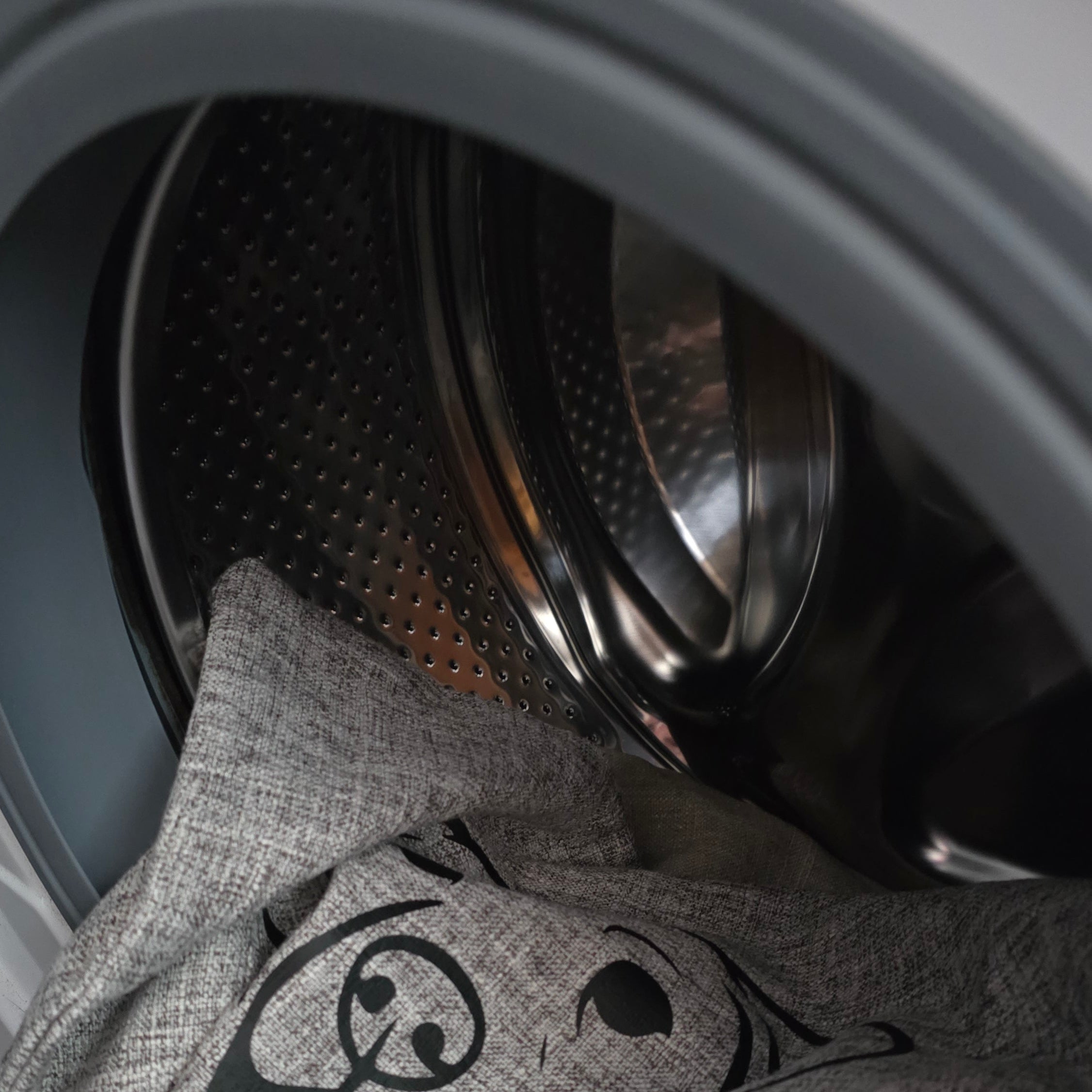 A close-up of a gray fabric bag with a black cartoon dog graphic, partially inside a washing machine drum.