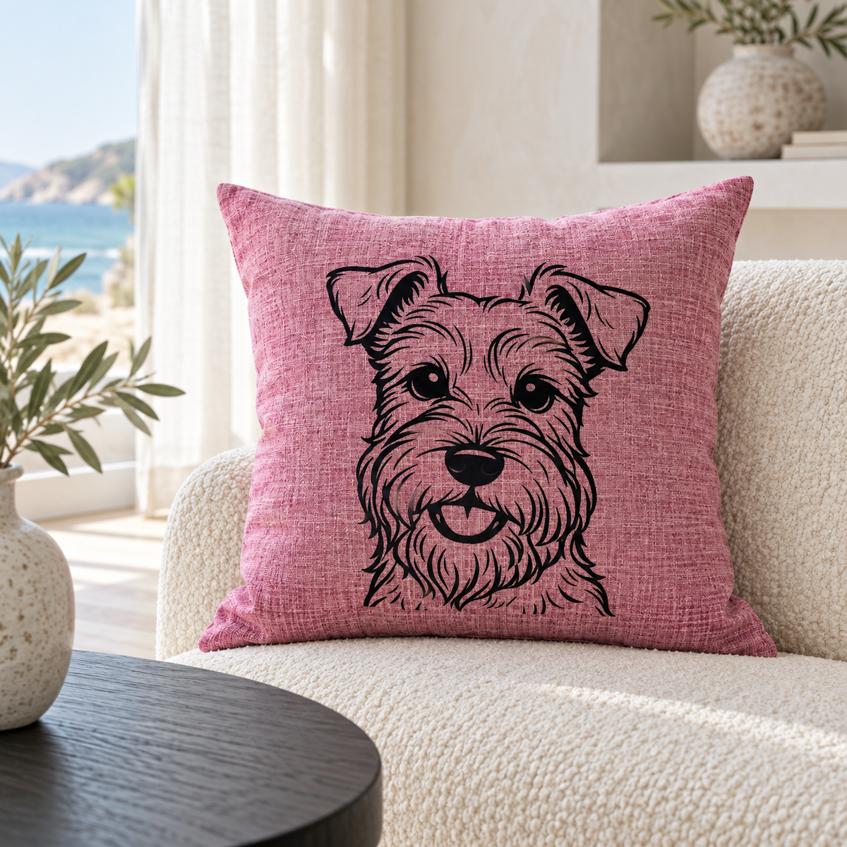 A square pink throw pillow with a black line art sketch of a schnauzer dog, resting on a cream-colored textured sofa in a bright, modern living room.