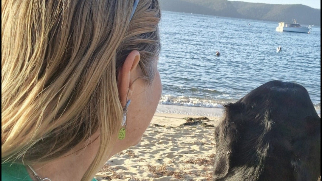 Woman and black dog on a beach looking at the ocean