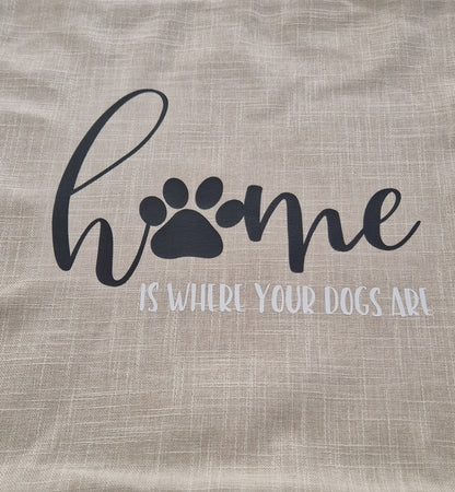 A beige cushion cover with the text 'Home is Where Your Dogs Are' and a paw print design on a sofa - dog gift, Australia by Rieko's World