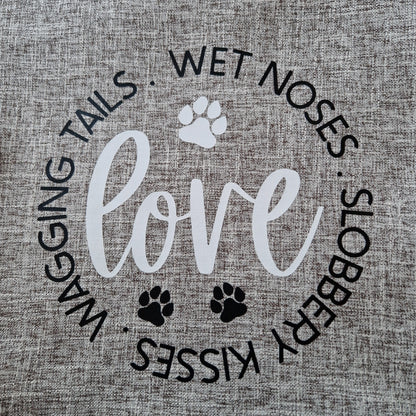 A light grey cushion cover with the word 'love' and dog-related phrases such as 'wagging tails', 'wet noses', and 'slobbery kisses' printed on it, along with paw prints - dog gift in Australia made by Rieko's World.