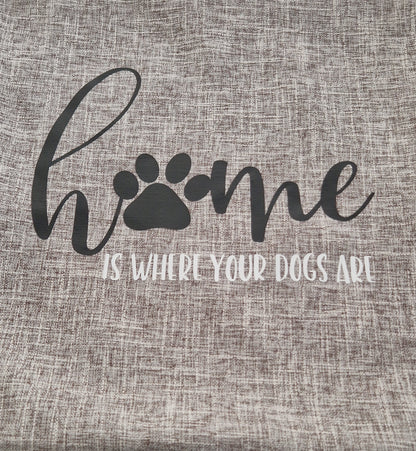 A grey cushion cover with the text 'Home is Where Your Dogs Are' and a paw print design on a sofa - dog gift, Australia by Rieko's World 