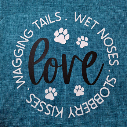 A teal cushion cover with the word 'love' and dog-related phrases such as 'wagging tails', 'wet noses', and 'slobbery kisses' printed on it, along with paw prints  - dog gift in Australia made by Rieko's World.